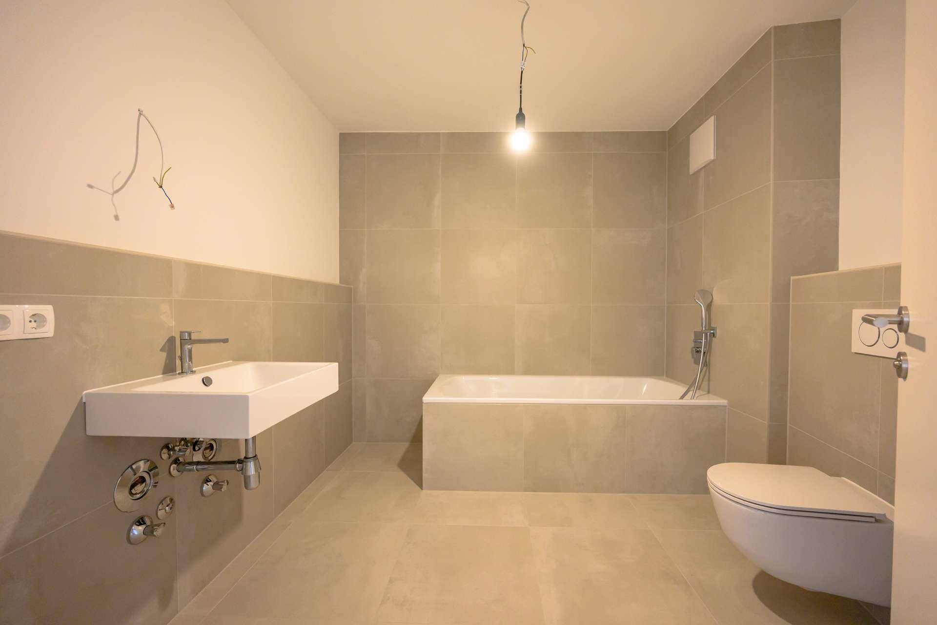 Modernes Badezimmer mit beigefarbenen Fliesen, einer Badewanne, einem Waschbecken und einem wandhängenden WC.