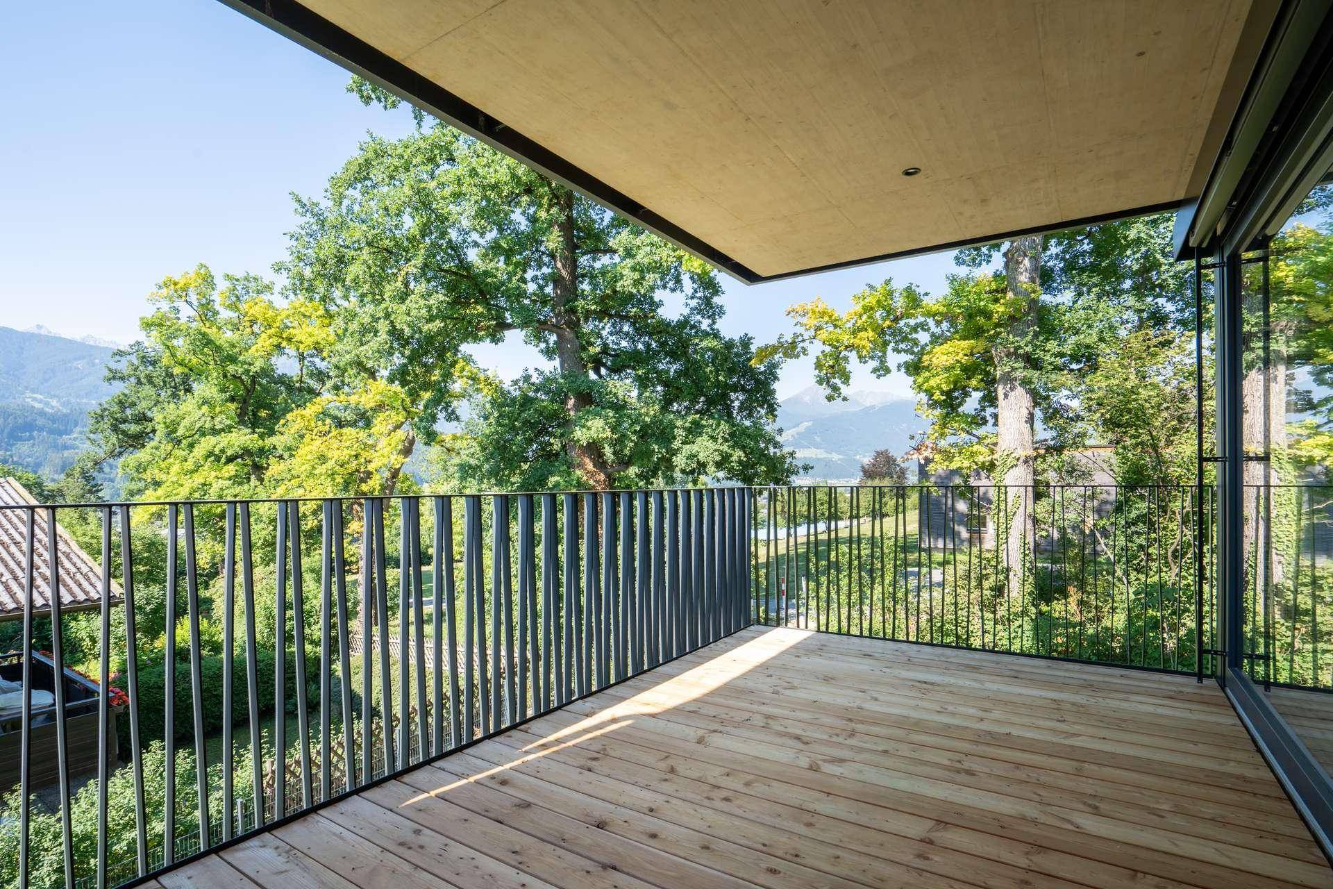 Geräumiger Balkon mit Holzboden und schwarzem Geländer, umgeben von üppigem Grün und Bergblick.