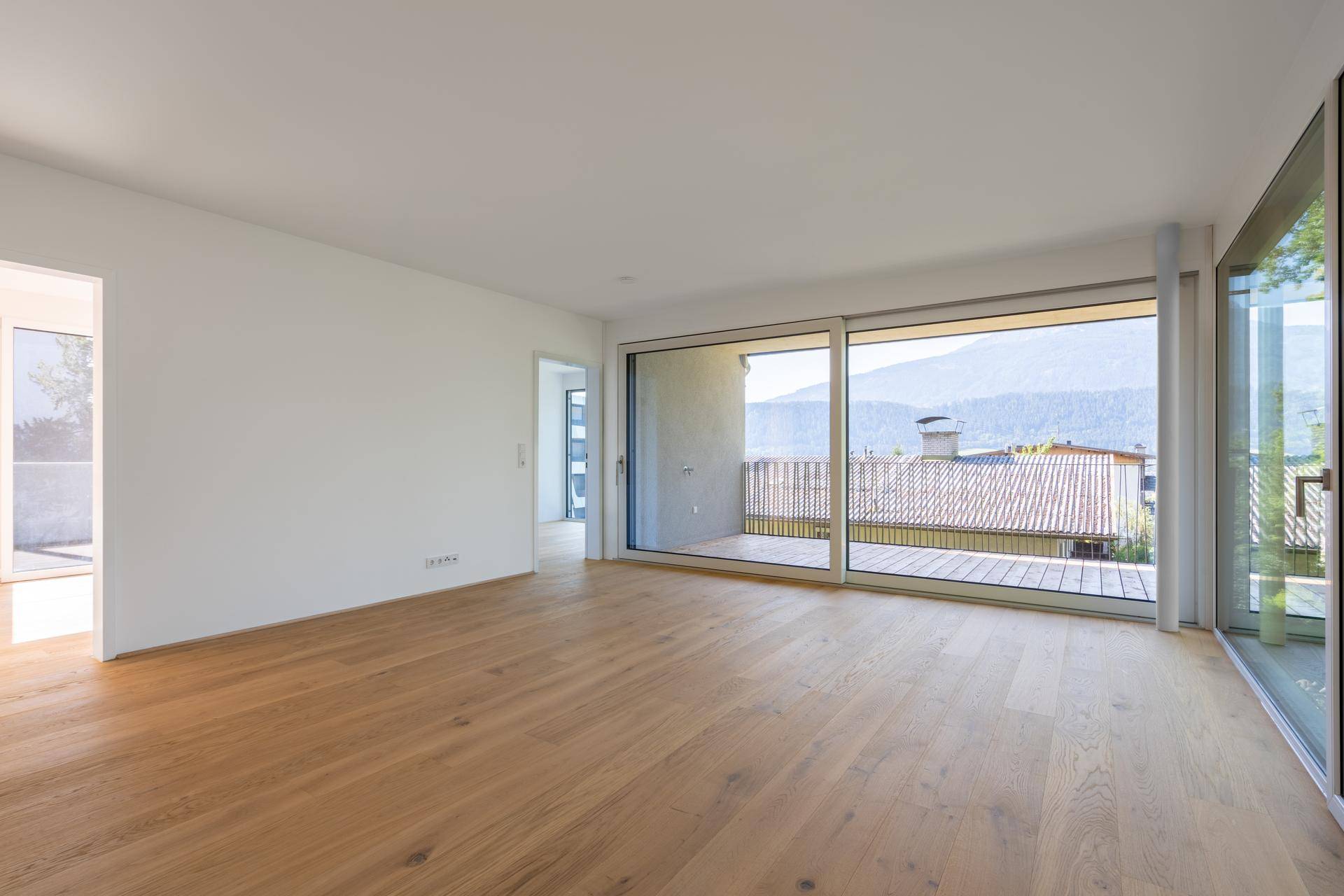 Geräumiges Zimmer mit Holzboden und Schiebetür zum Balkon, mit Blick auf die Berge.