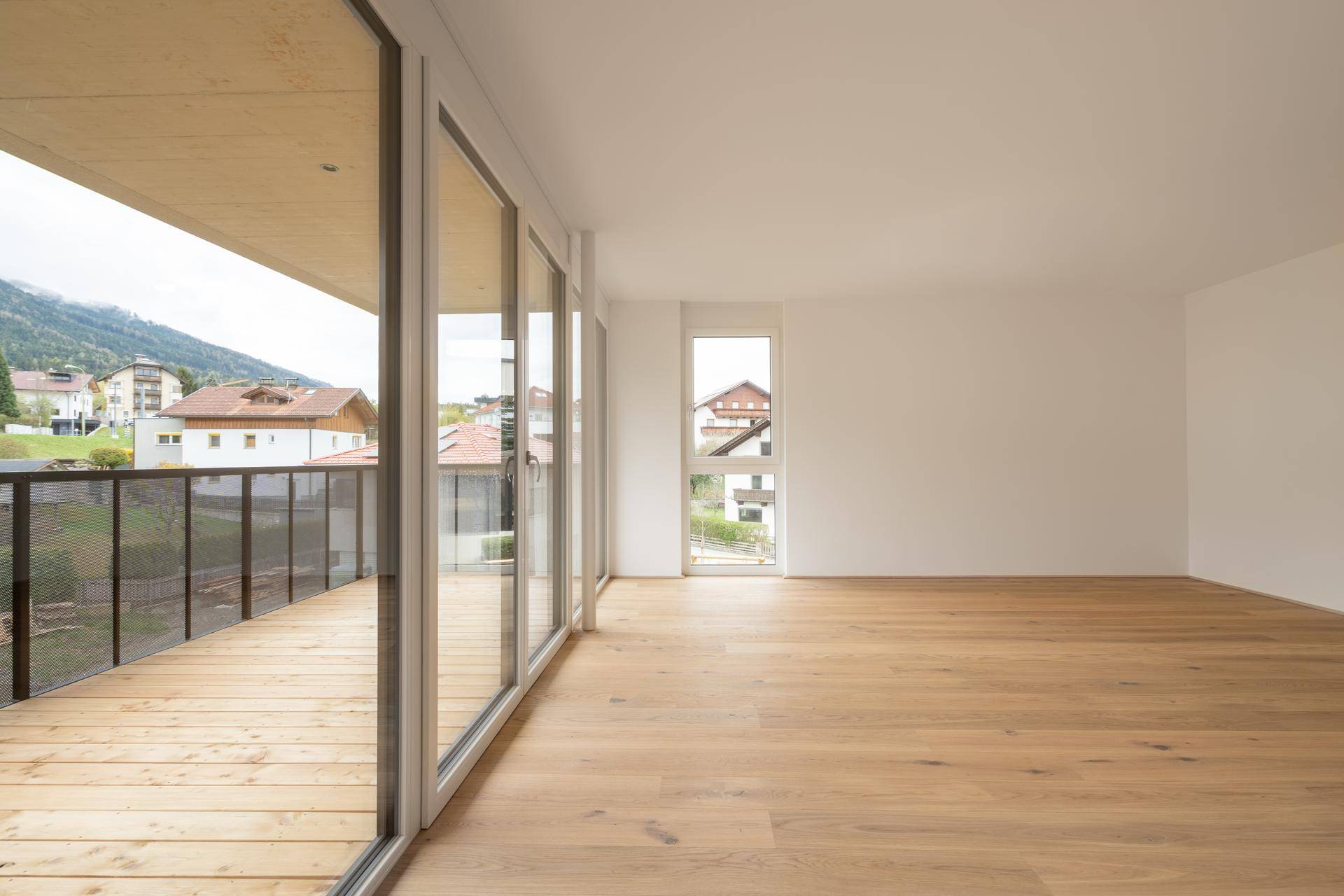 Lichtdurchfluteter Wohnbereich mit Holzboden und breiter Fensterfront zum Balkon mit Bergsicht.