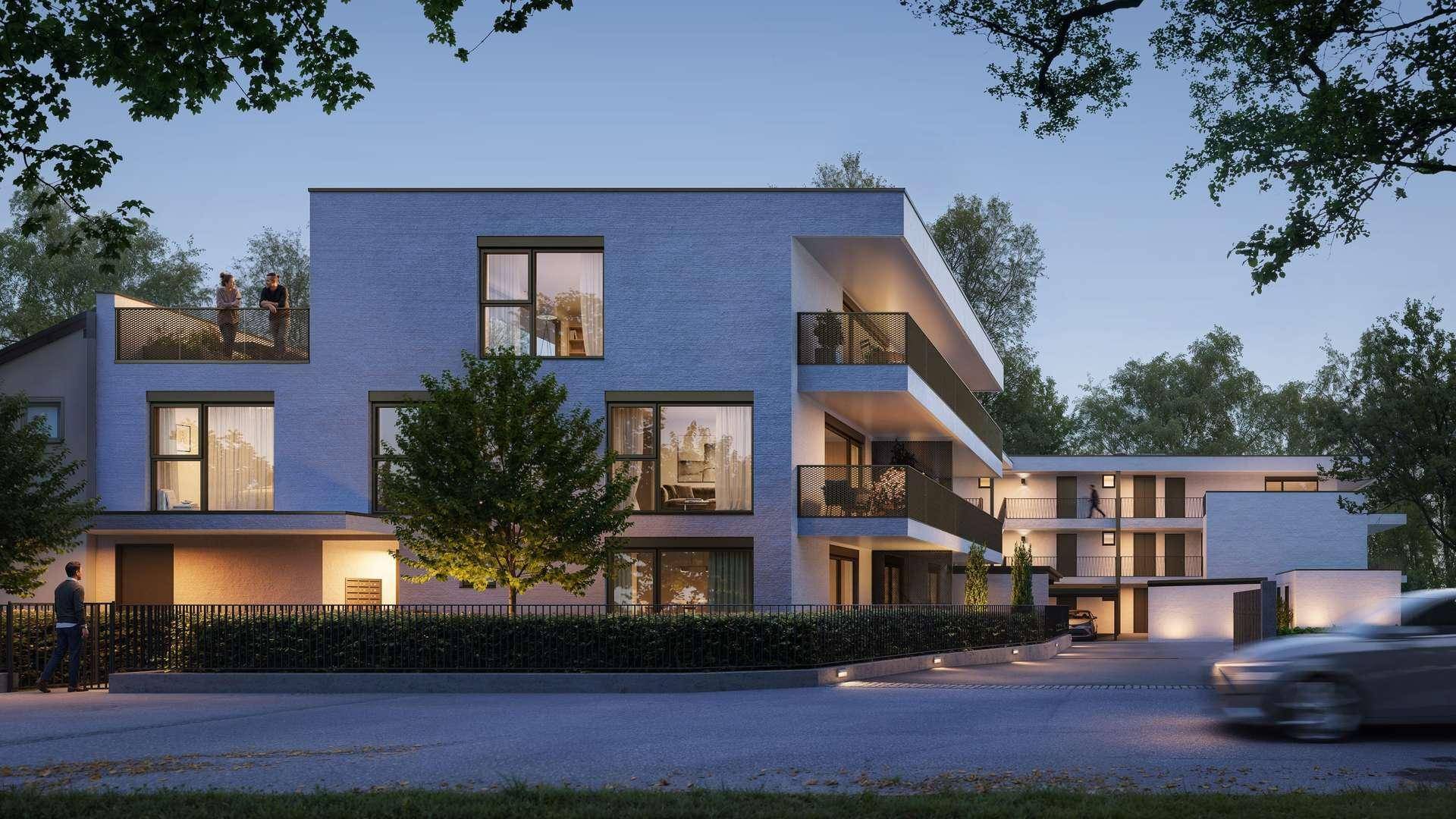 Moderne Wohnanlage bei Dämmerung mit beleuchteten Balkonen und Zufahrt.