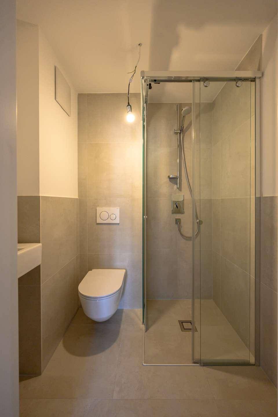 Zeitgemäßes Badezimmer mit beigefarbenen Fliesen, einer geräumigen Duschkabine und einem wandhängenden WC.