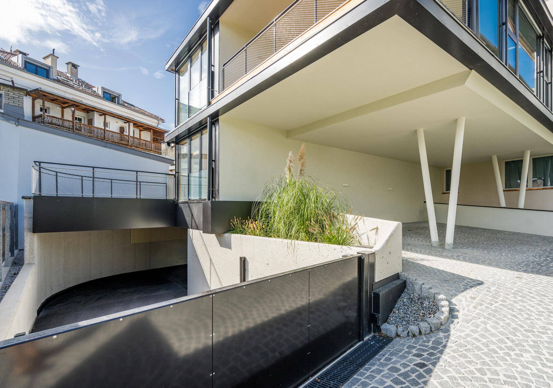 Zufahrt zur Tiefgarage mit moderner Architektur und gepflastertem Vorplatz.