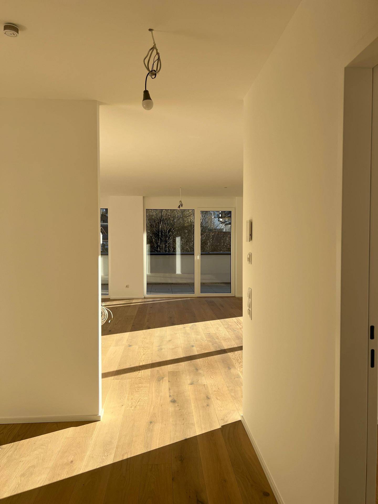 Heller Flur mit Holzboden, der zu einem weiteren Raum mit großen Fenstern und viel Sonnenlicht führt.