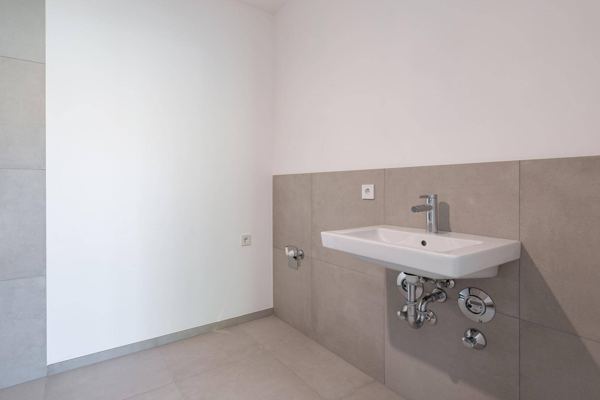 Modernes Badezimmer mit Waschbecken, grauen Fliesen und weißen Wänden.