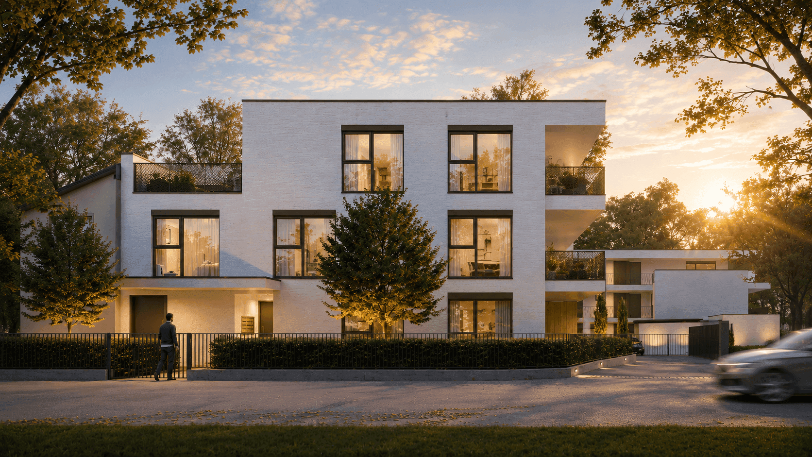 Moderne Wohnanlage bei Sonnenuntergang mit weißer Fassade, großen Fenstern und Bäumen.