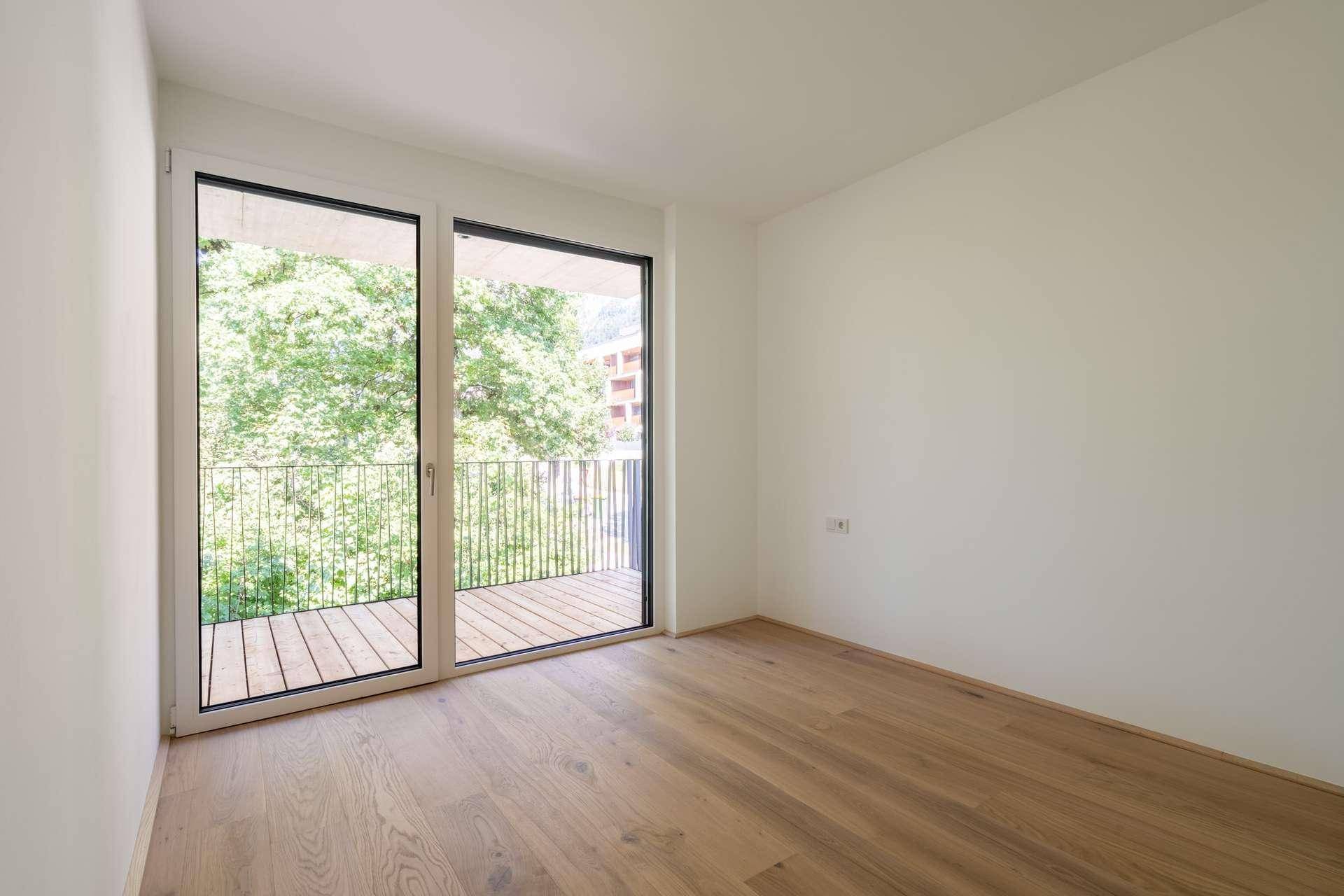 Lichtdurchflutetes Schlafzimmer mit Holzboden und raumhoher Verglasung, die den Blick ins Grüne freigibt.