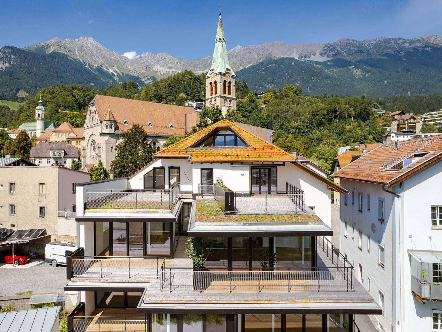 Moderne Architektur mit mehreren Terrassen und Blick auf die Berge und eine Kirche.