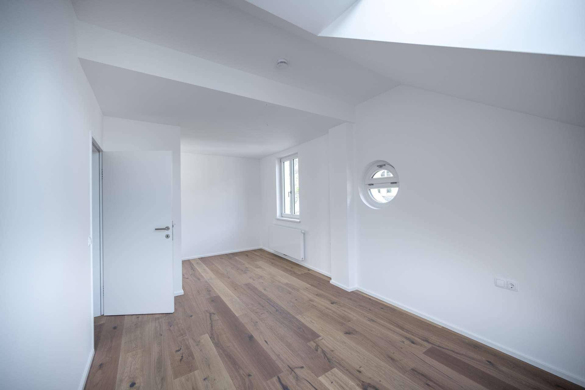Helles Zimmer mit Holzboden, weiß gestrichenen Wänden und einem einzigartigen runden Fenster.