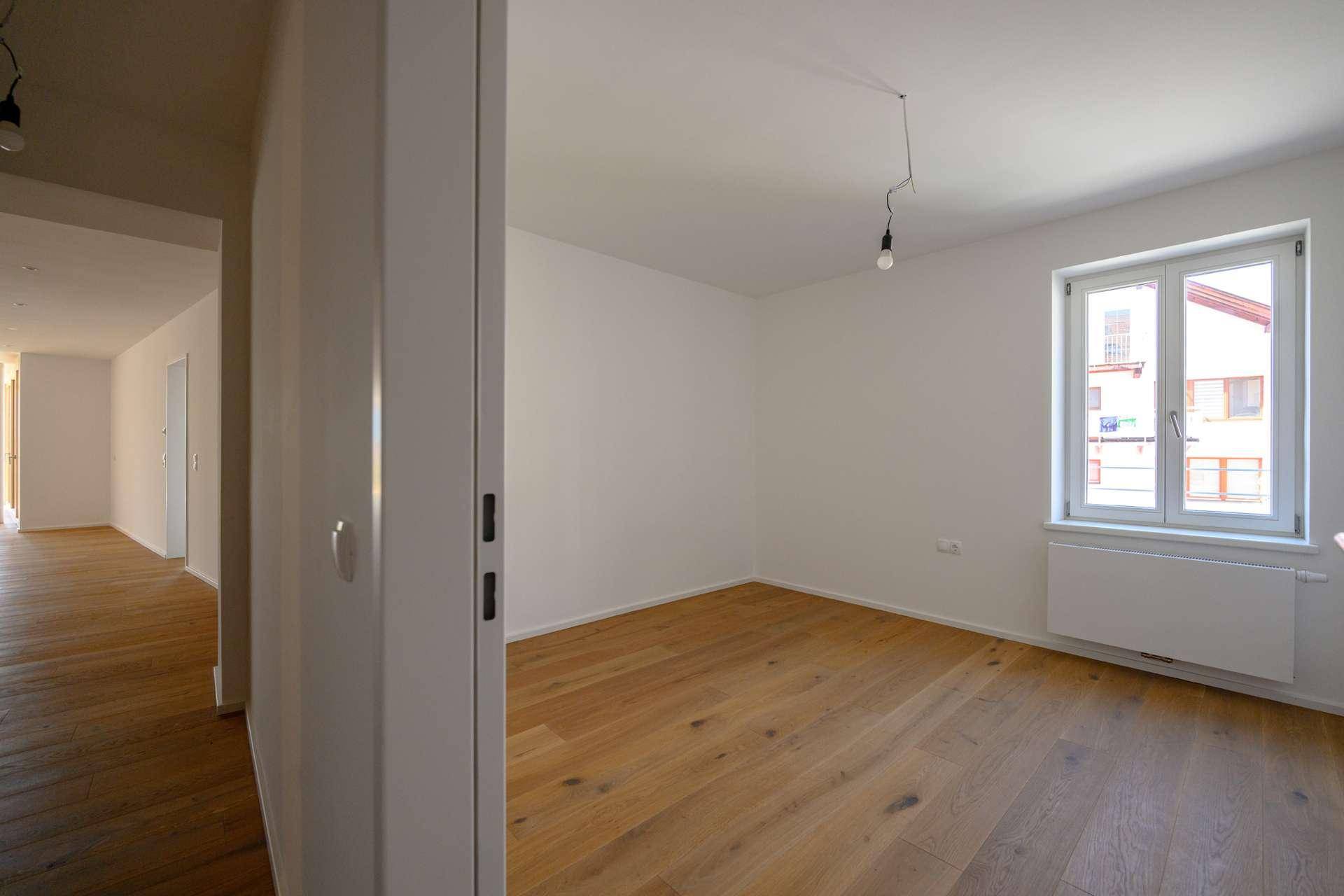 Helles, leeres Zimmer mit Holzboden und einem Fenster, ideal als Schlafzimmer oder Büro nutzbar.