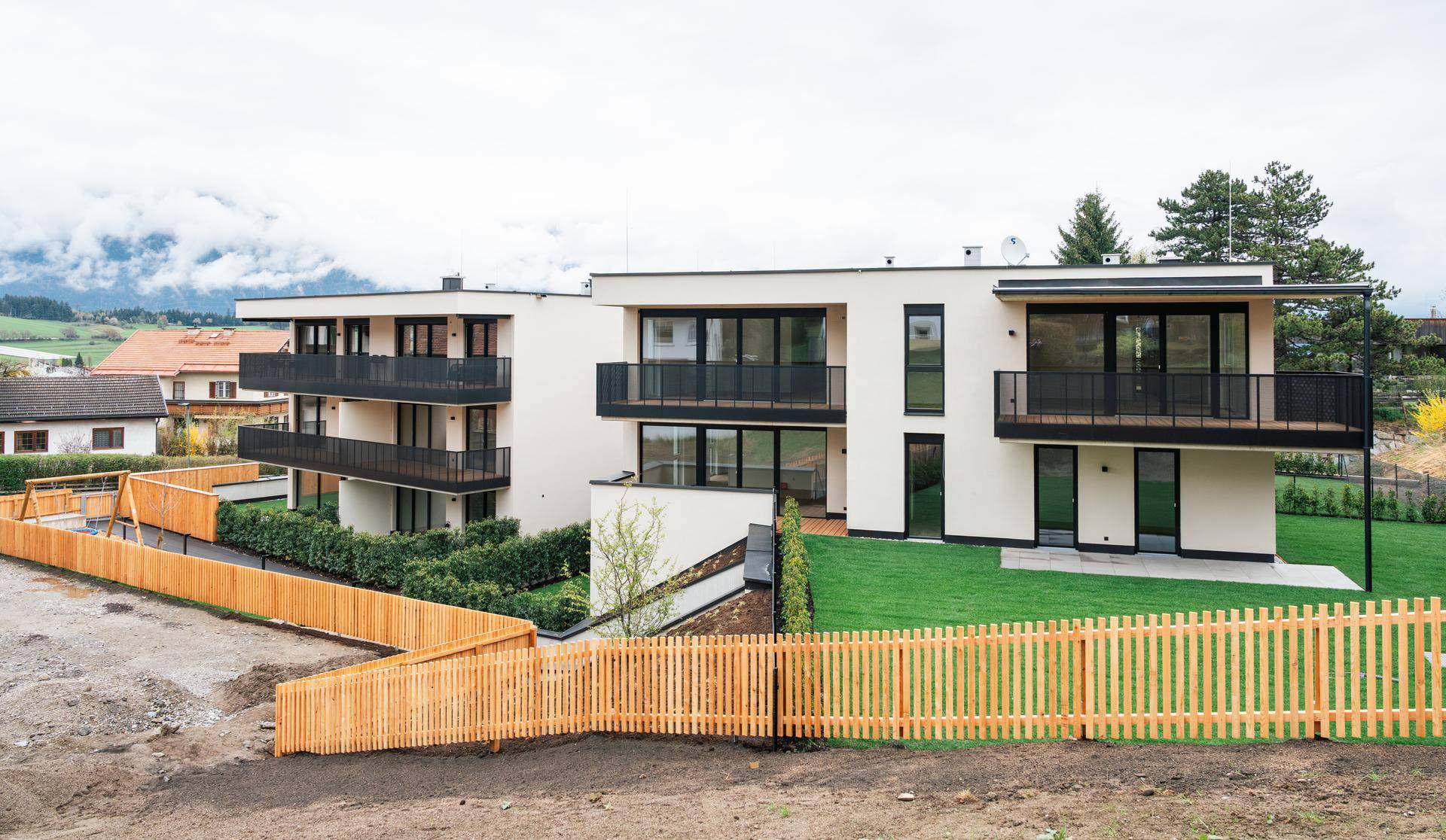 Moderne Wohngebäude mit Balkonen, gepflegtem Rasen und Bergblick in ländlicher Umgebung.