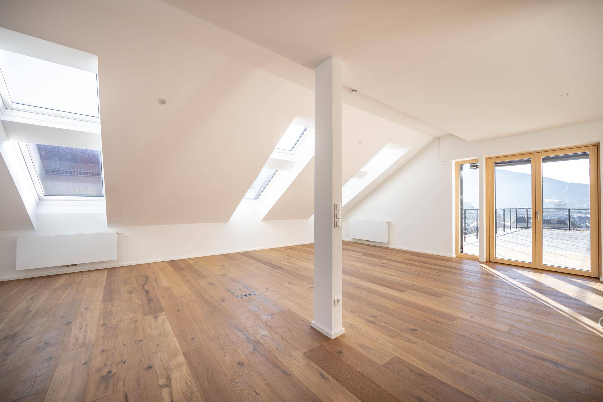 Helles, geräumiges Wohnzimmer mit Holzboden, Dachschrägen und Zugang zur Terrasse.