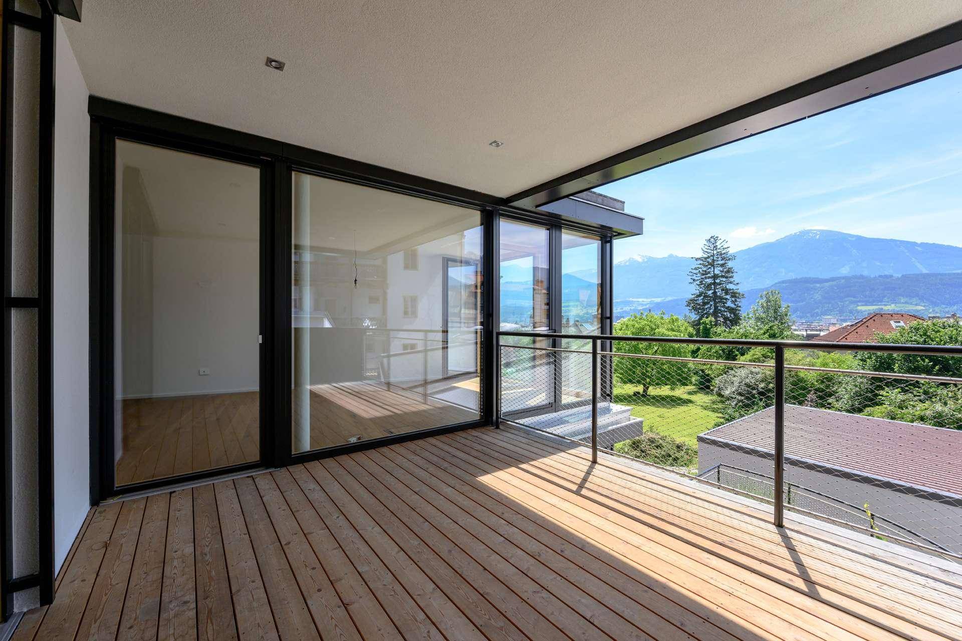 Geräumiger Balkon mit Holzdielen und Glasgeländer, bietet einen beeindruckenden Blick auf die umliegende Berglandschaft.