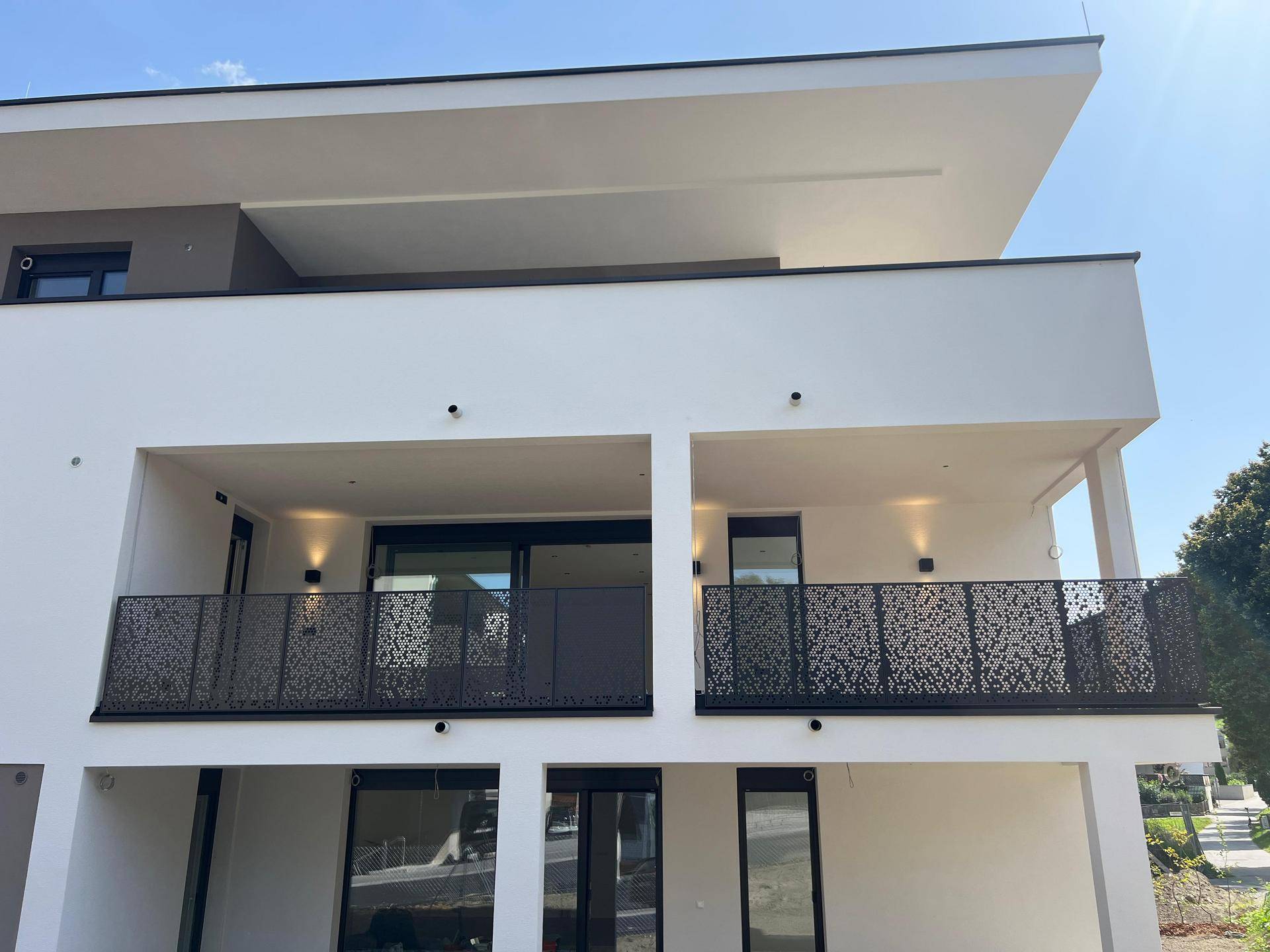 Moderne Balkone mit dekorativen Metallgeländern an der weißen Fassade eines Neubaus bei Sonnenschein.