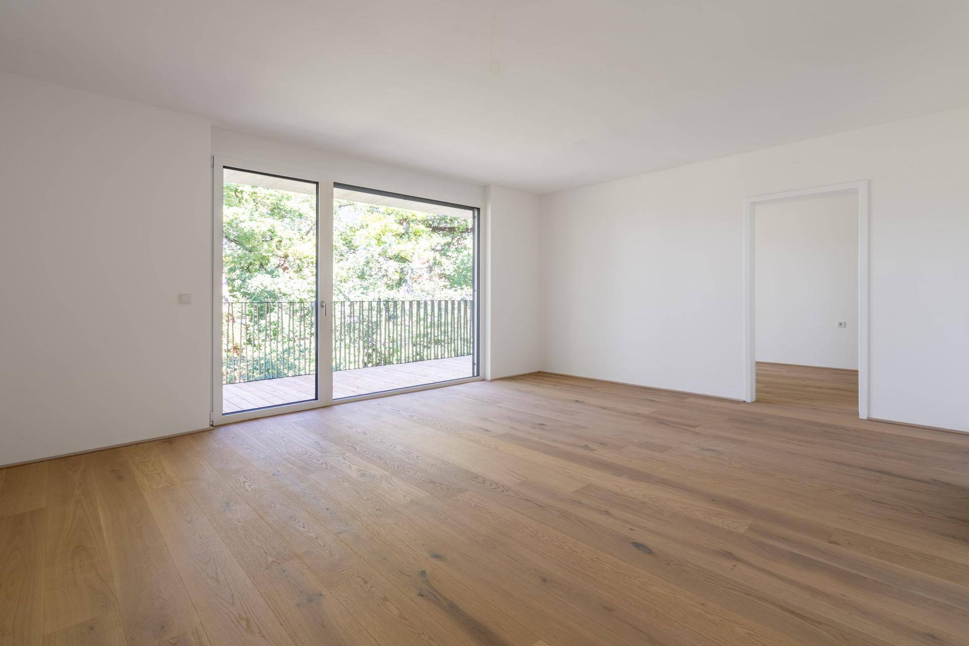 Geräumiges, helles Zimmer mit Holzboden und großen Fenstern zum Balkon.