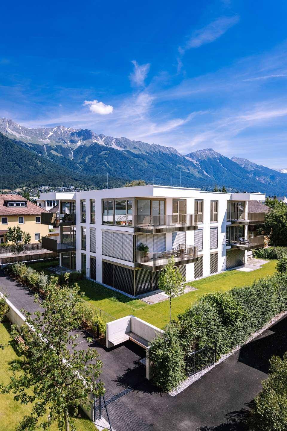 Luftaufnahme einer modernen Wohnanlage mit mehreren Gebäuden, Balkonen und Bergblick.