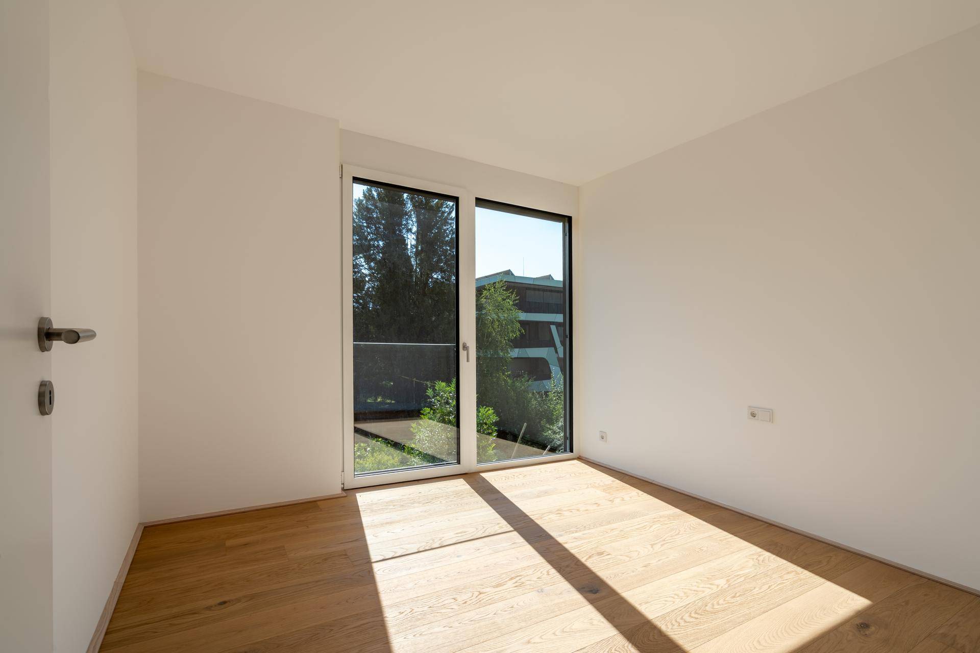 Sonniger Raum mit Holzboden und Fenster, das viel natürliches Licht hereinlässt.