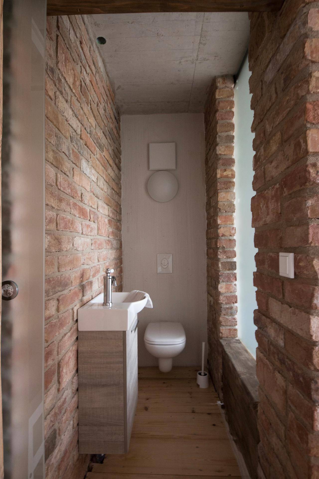 Schmale Gästetoilette mit Waschbecken, WC und charakteristischen Ziegelwänden.