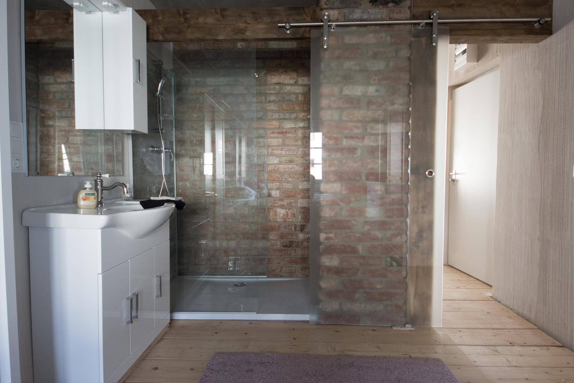 Modernes Badezimmer mit begehbarer Dusche, Waschbecken und freiliegender Ziegelwand.