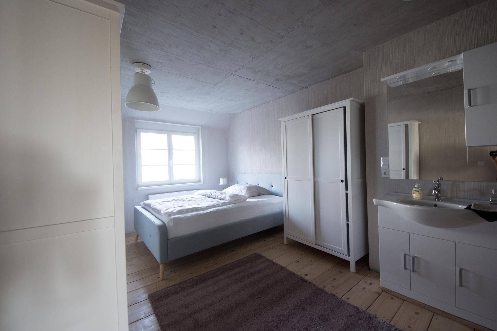 Helles Schlafzimmer mit Holzboden, Kleiderschrank und integriertem Waschbeckenbereich.
