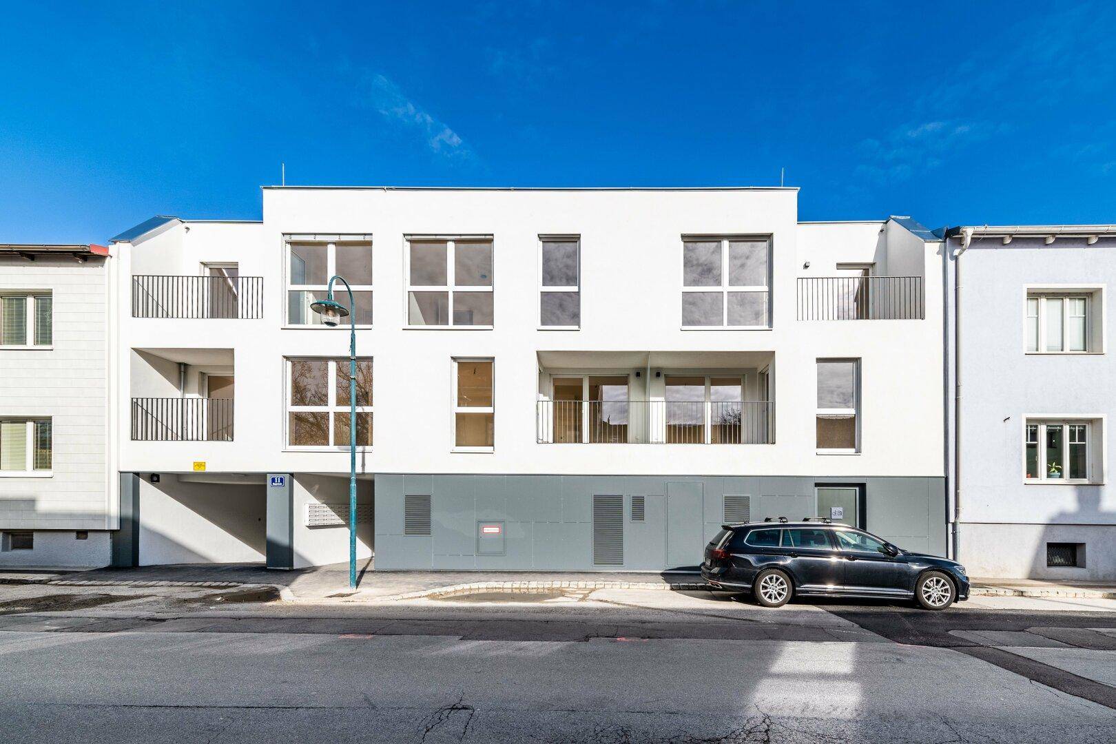 Moderne Wohnhausfassade mit großen Fenstern und Balkonen an einer städtischen Straße.