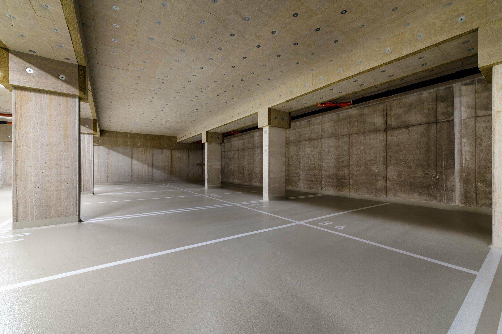 Saubere Tiefgarage mit Betonwänden und -säulen sowie markierten Parkflächen.