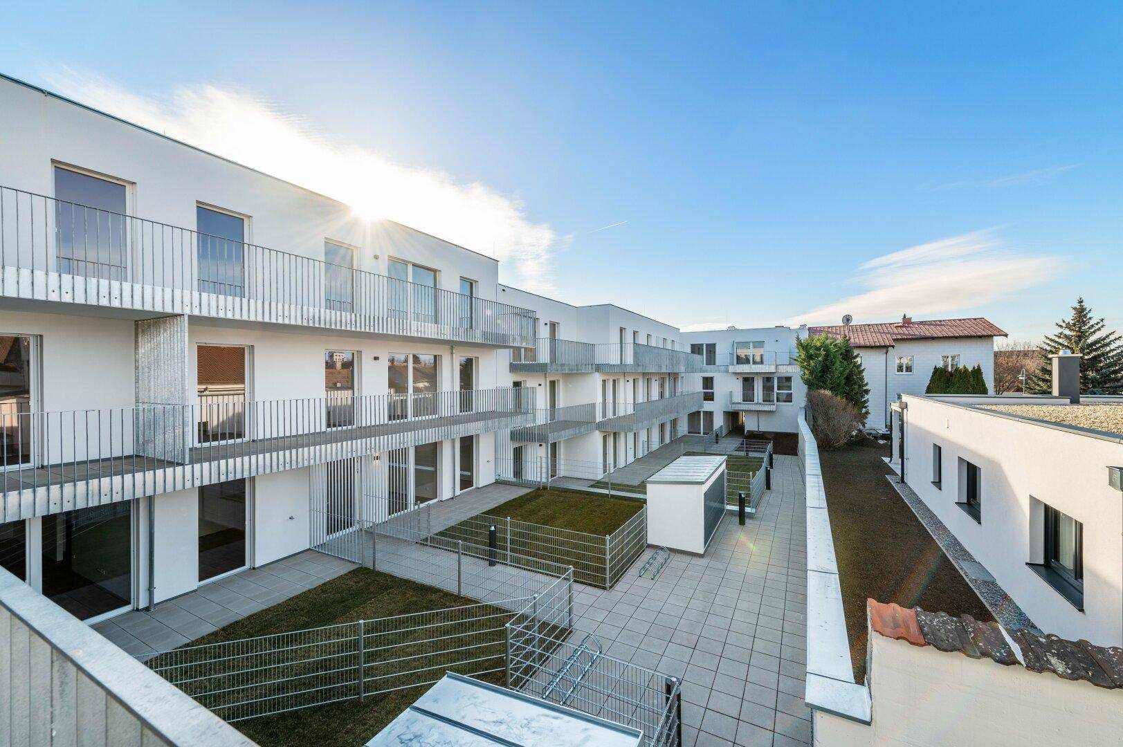Innenhofansicht eines modernen Wohnkomplexes mit Balkonen, Terrassen und Grünflächen.