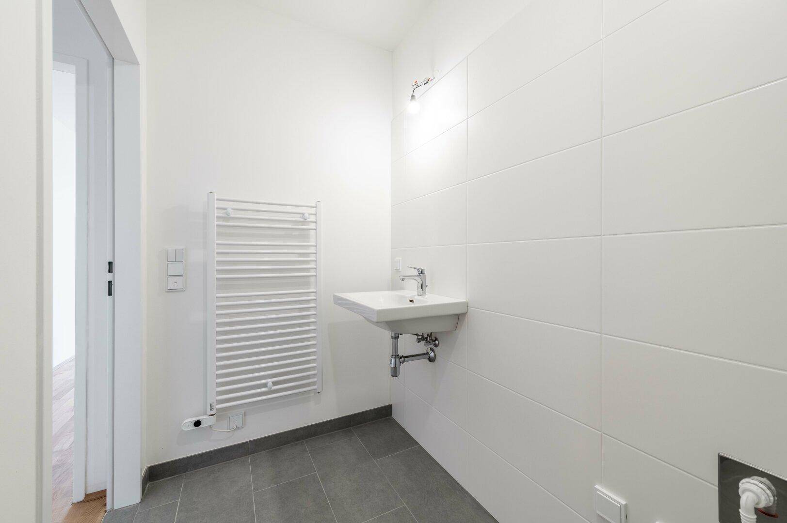 Helles Badezimmer mit Waschbecken, beheiztem Handtuchhalter und weißen Fliesen.