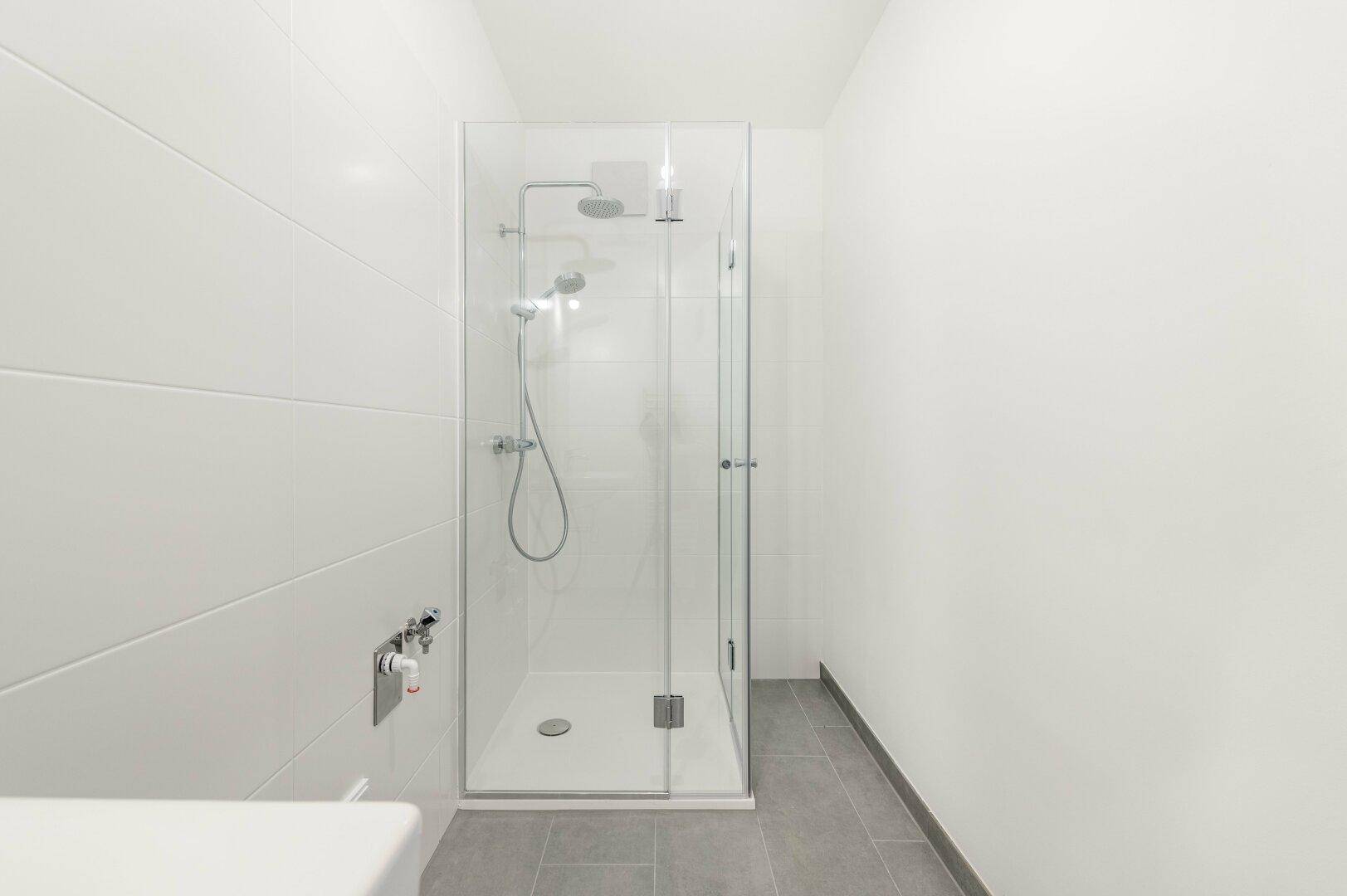 Sauberes Badezimmer mit moderner Duschkabine und weißen Wand- und grauen Bodenfliesen.