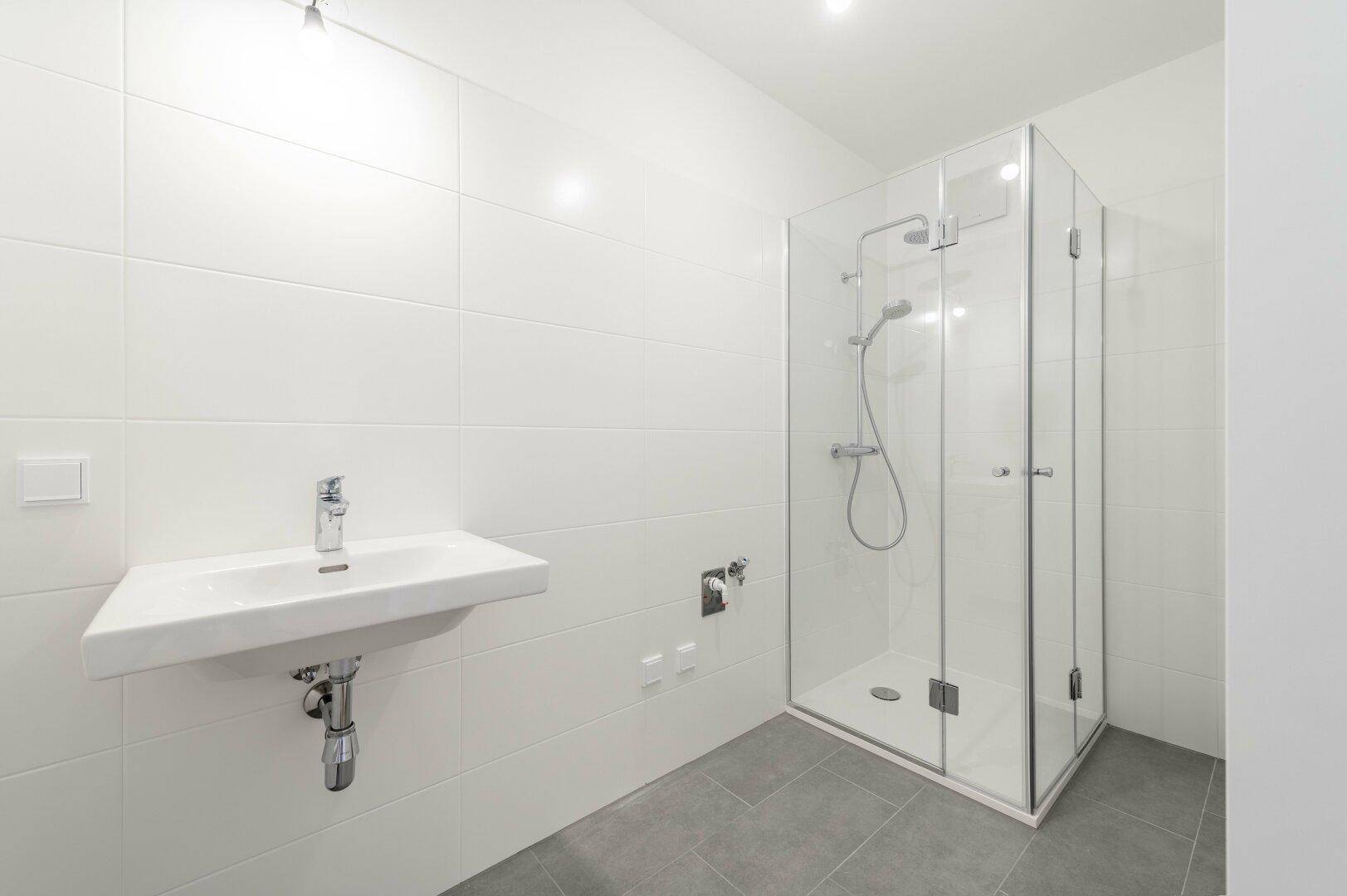 Modernes Badezimmer mit Duschkabine, Waschbecken und weißen Wand- und grauen Bodenfliesen.