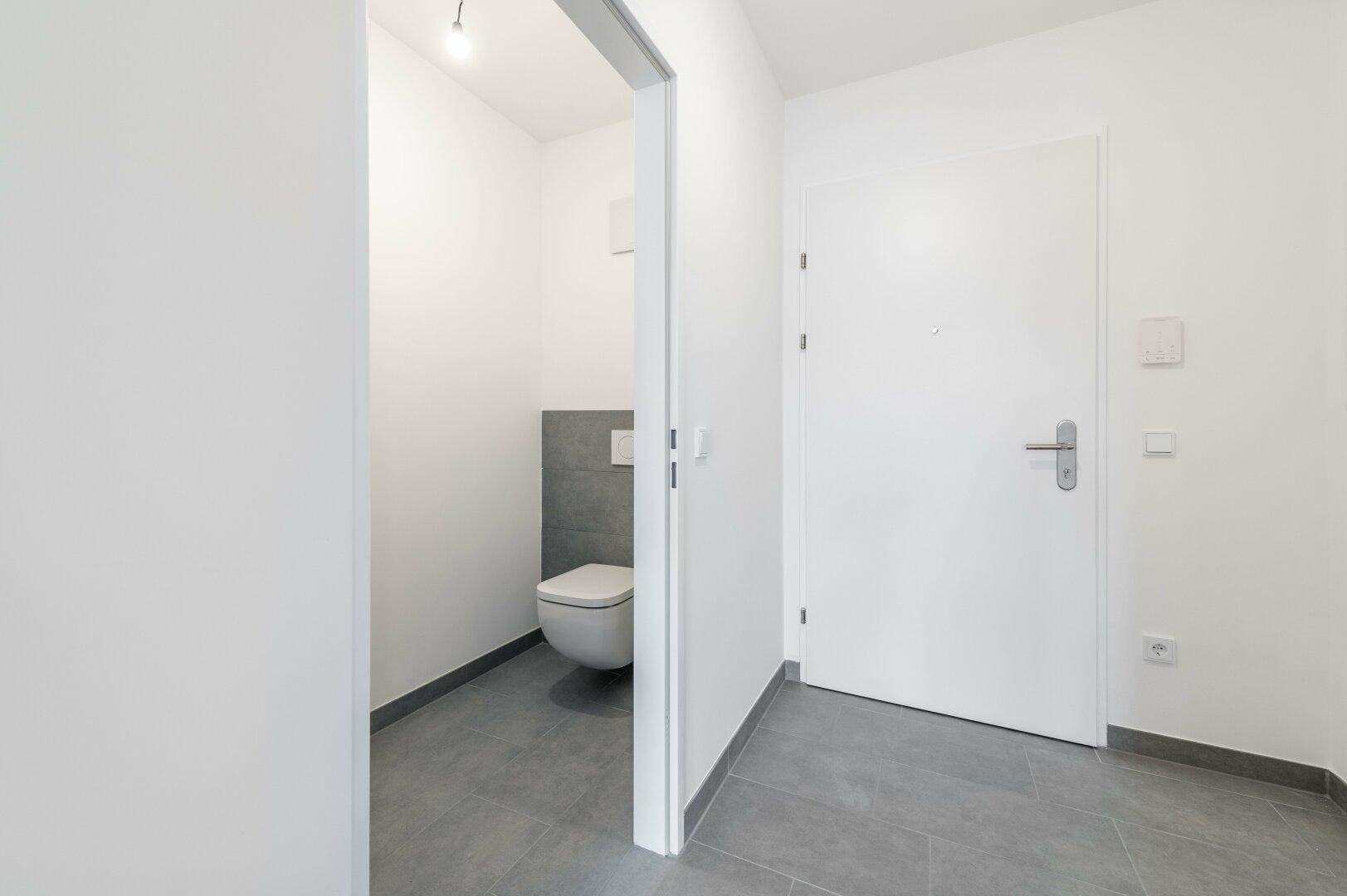 Flur mit Zugang zu einem modernen Gäste-WC, ausgestattet mit Wand-WC und Fliesen.