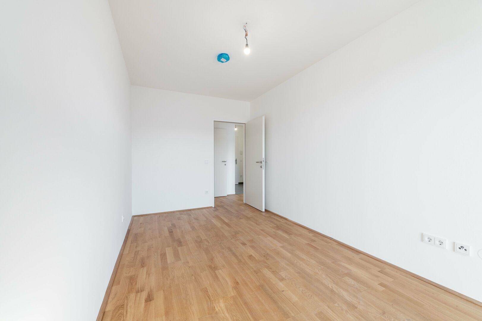 Heller, leerer Raum mit Holzboden und weißen Wänden, bereit zur individuellen Gestaltung.