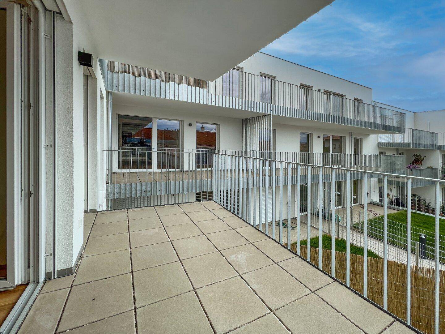 Heller Balkon mit Metallgeländer und Blick auf die modernen Fassaden und den begrünten Innenhof.
