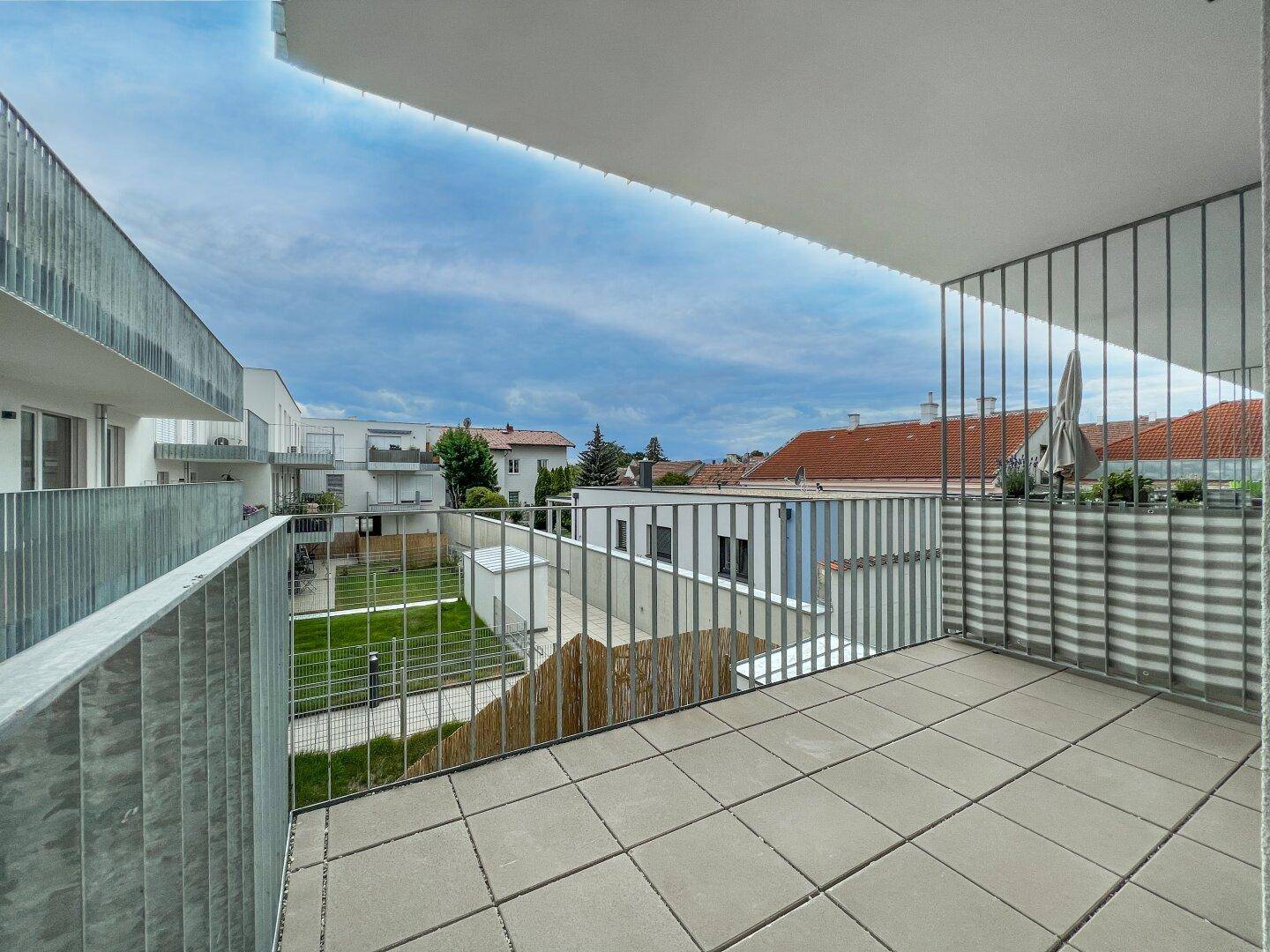 Geräumiger Balkon mit Fliesenboden und Blick auf den Innenhof und umliegende Gebäude.