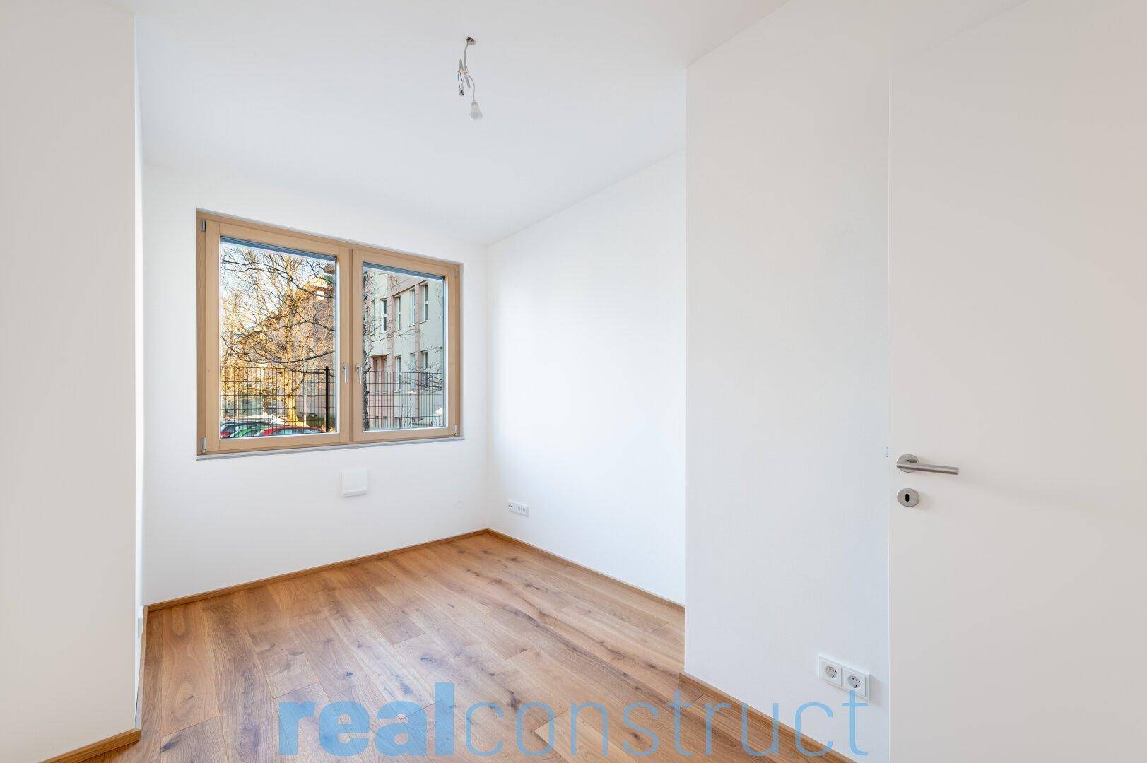 Helles Schlafzimmer mit Holzboden und Fensterblick ins Grüne.
