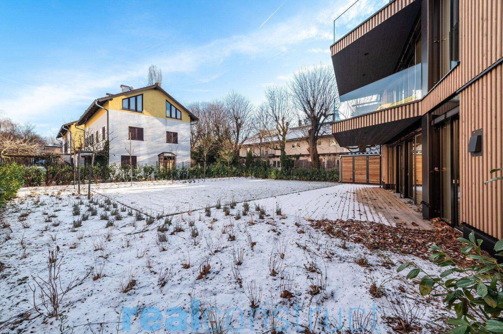 Gartenbereich mit junger Bepflanzung und angrenzender Terrasse im Winter.