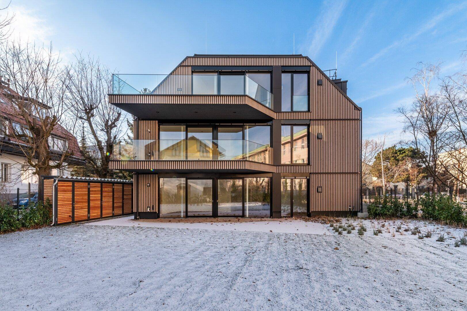 Rückansicht des modernen Gebäudes mit Holzfassade und Gartenbereich im Winter.