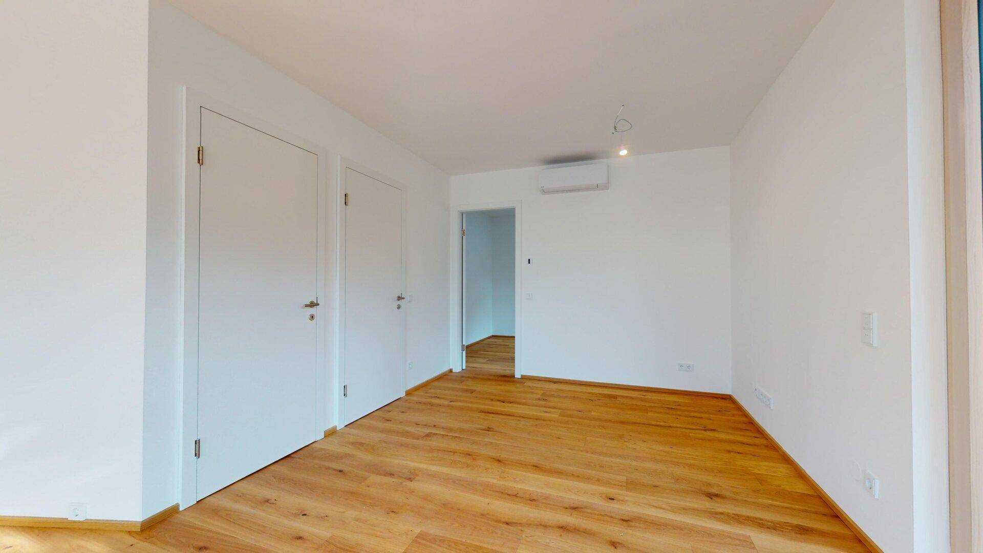 Leeres Zimmer mit Holzboden, weißen Wänden und einer Klimaanlage, bereit zur Einrichtung.