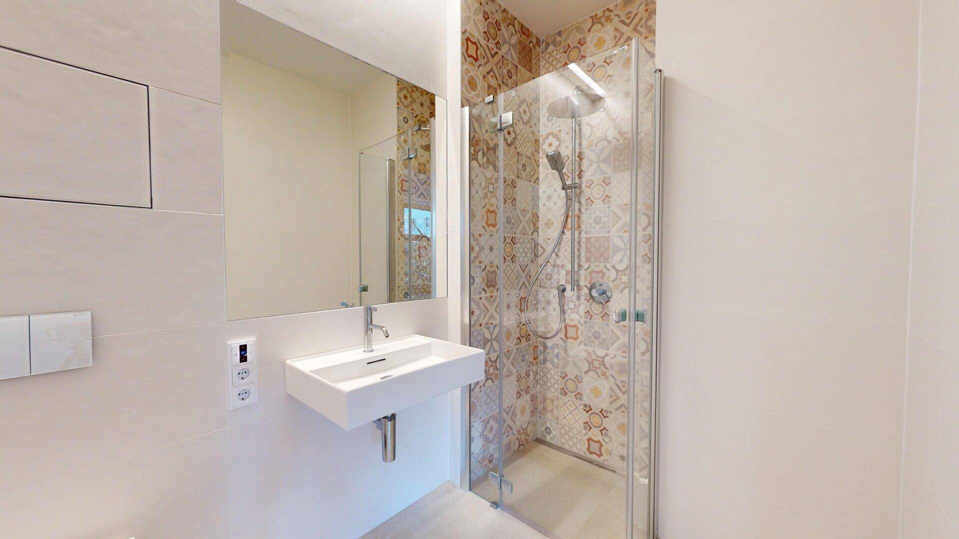 Modernes Badezimmer mit Duschkabine, Einzelwaschbecken und dekorativen Fliesen an der Wand.