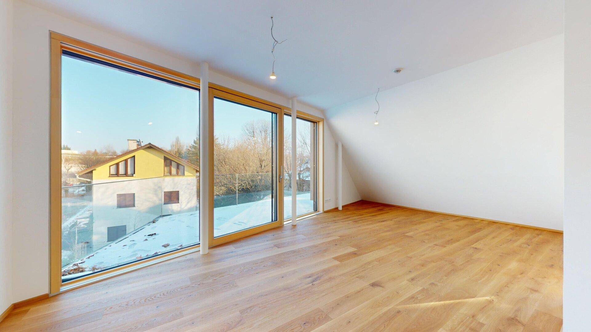 Lichtdurchfluteter Raum mit Holzboden und großen Fenstern, die einen weiten Blick nach draußen bieten.