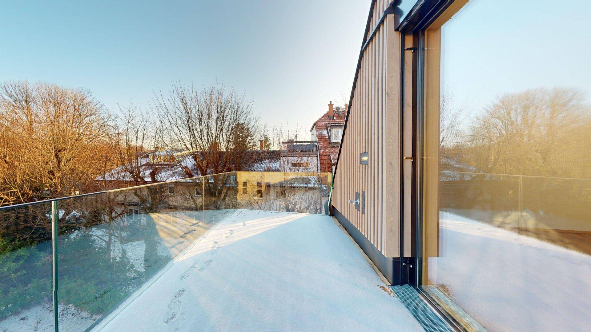 Geräumige Terrasse mit Glasgeländer und Blick auf die umliegende Bebauung an einem sonnigen Wintertag.