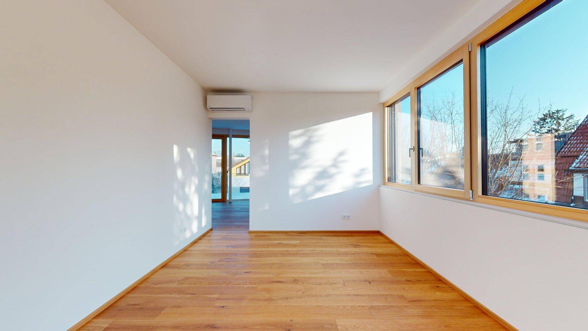 Heller Raum mit Holzboden, großen Fenstern und einer Klimaanlage an der Wand für angenehmes Klima.