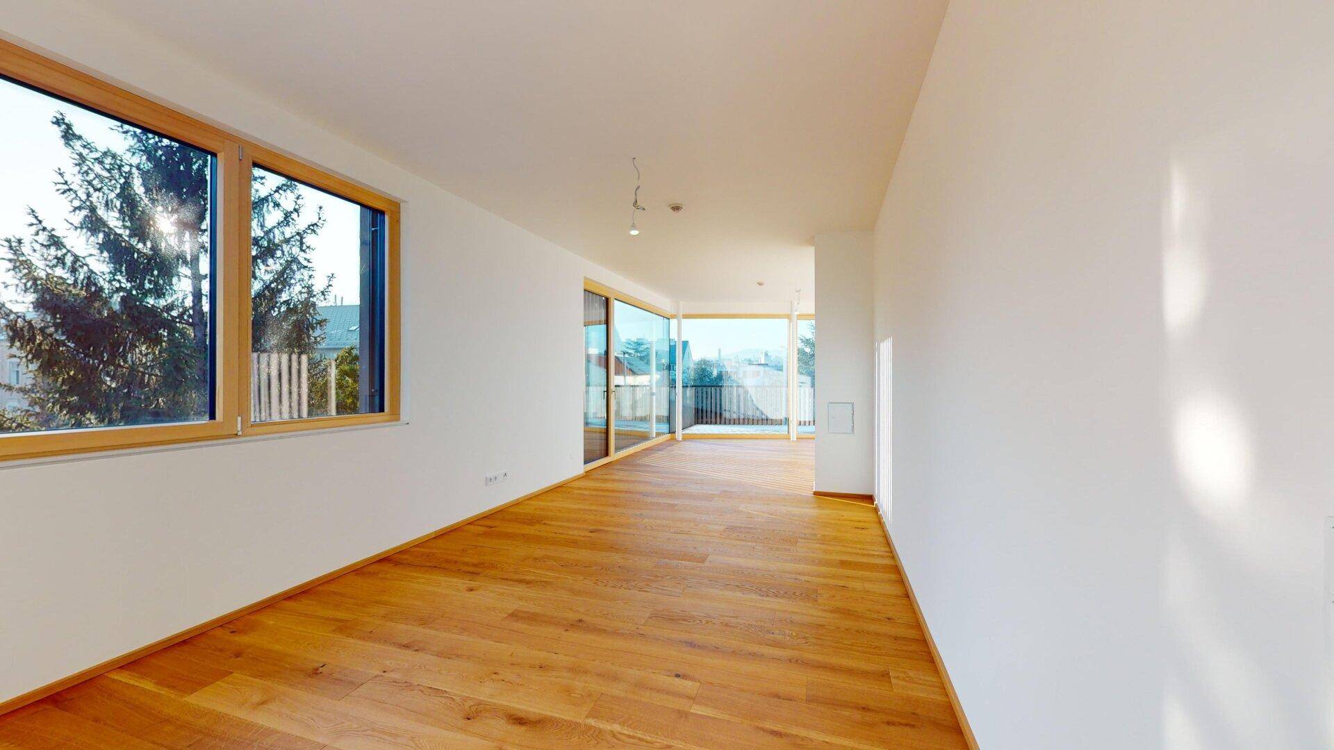 Langer, heller Raum mit Holzboden und großen Fenstern, die viel Tageslicht hereinlassen und Ausblick bieten.