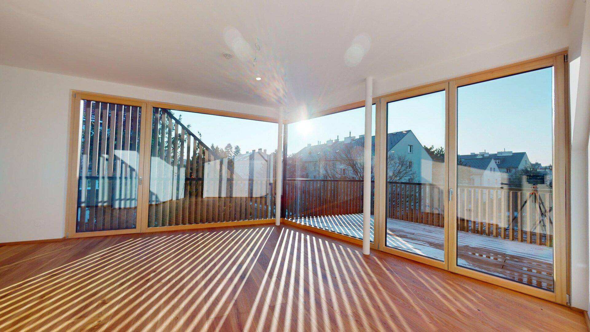 Heller Eckraum mit Holzboden und großen Fenstern, die viel Sonnenlicht hereinlassen und Ausblick bieten.