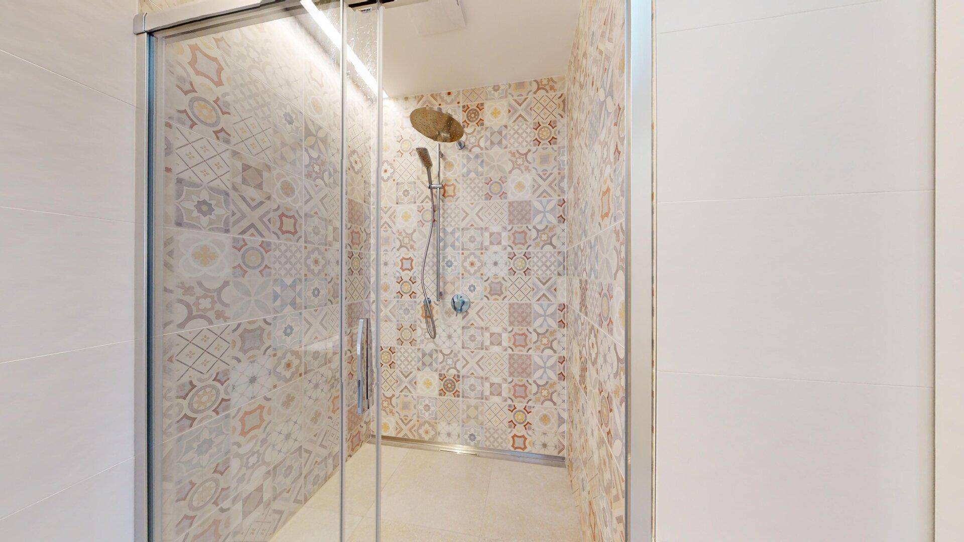 Moderne Duschkabine mit gemusterten Fliesen und einer Regendusche in einem hellen Badezimmer.