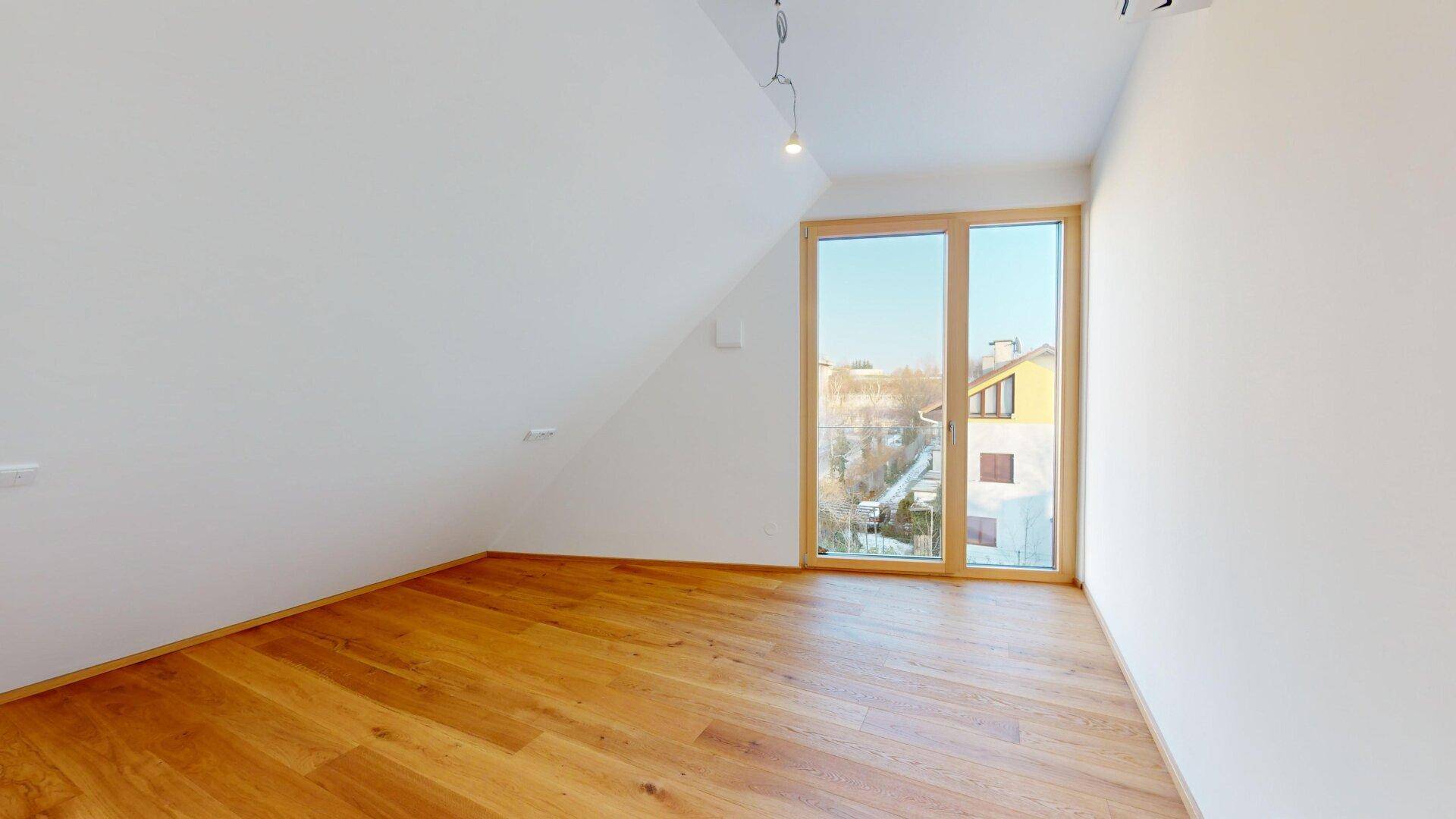 Heller Raum mit Holzboden, Dachschräge und großem Fenster mit weitem Blick nach draußen.
