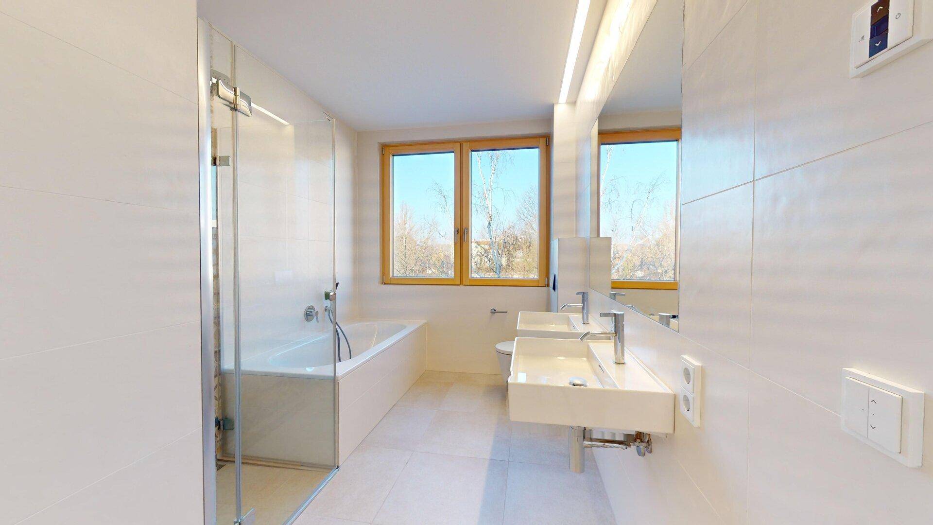 Modernes Badezimmer mit Doppelwaschbecken, Badewanne, Dusche und Fenster für natürliches Tageslicht.