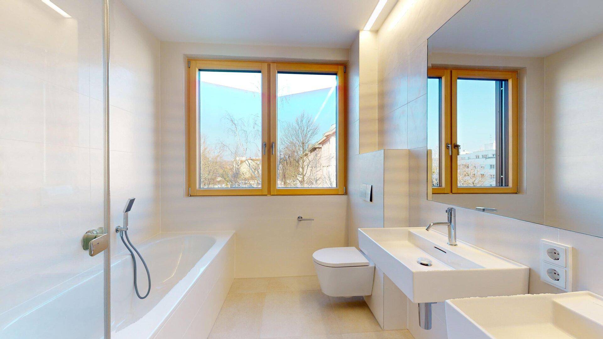 Helles Badezimmer mit Doppelwaschbecken, Badewanne, Toilette und großem Fenster für viel Licht.