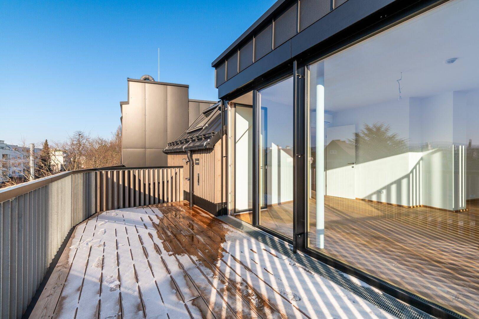Moderne Holzterrasse mit Blick auf das Gebäude und die Umgebung an einem klaren Wintertag.
