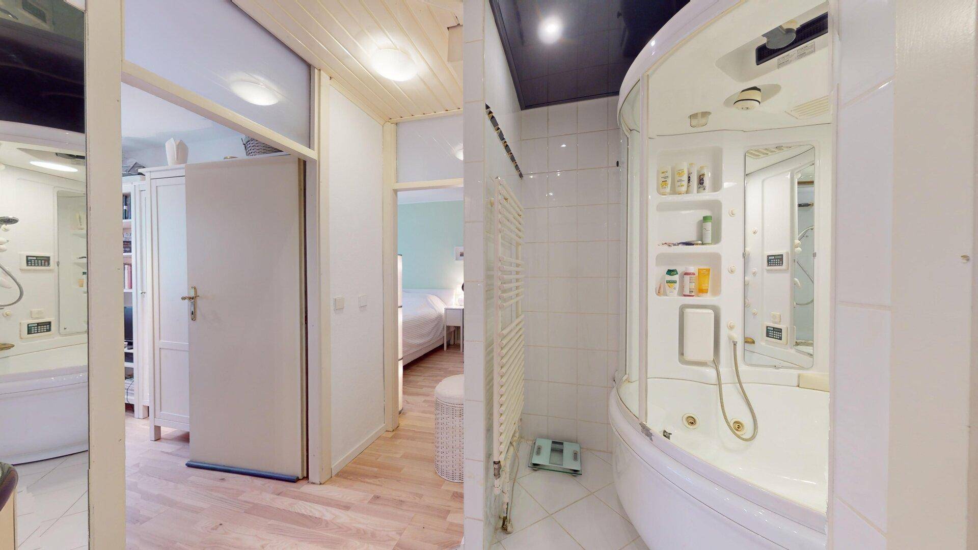 Badezimmer mit Duschkabine und Zugang zu einem weiteren Raum, hell gefliest und praktisch.